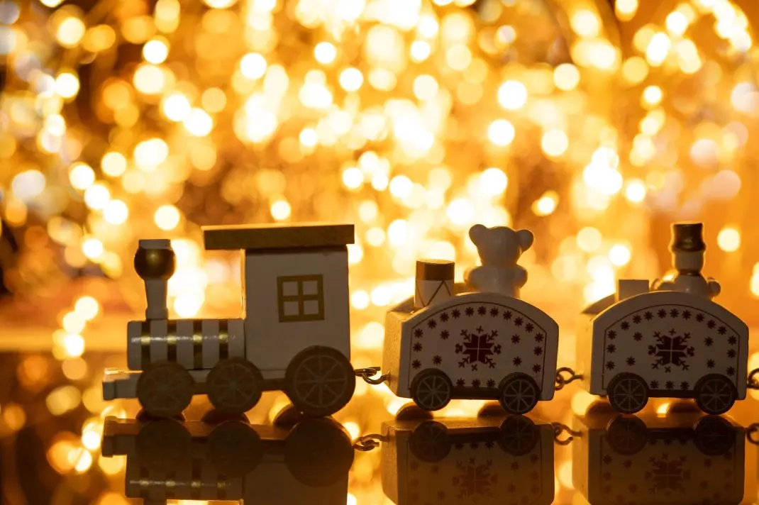 Travelling with AWC this Christmas: A wooden toy train in front of golden Christmas lights.