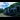 A blue train travelling along the Darjeeling Himalayan Railway through green hills and under a cloudy blue sky