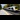 West Coast Train Line: A train speeds past an empty platform, with trees on one side of the station.