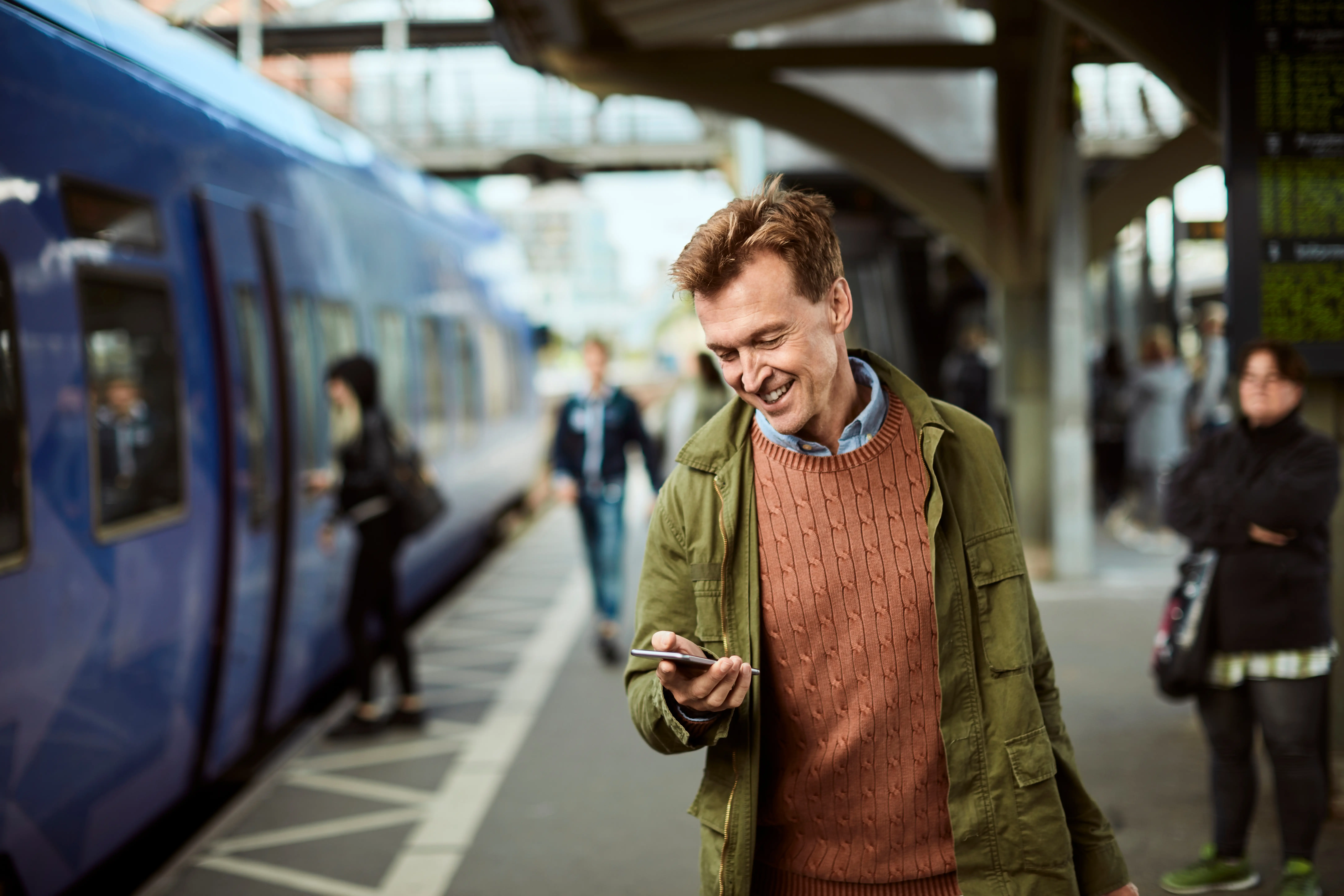 Train Departure Boards: A man smiles as he looks at his phone, ready to board a train