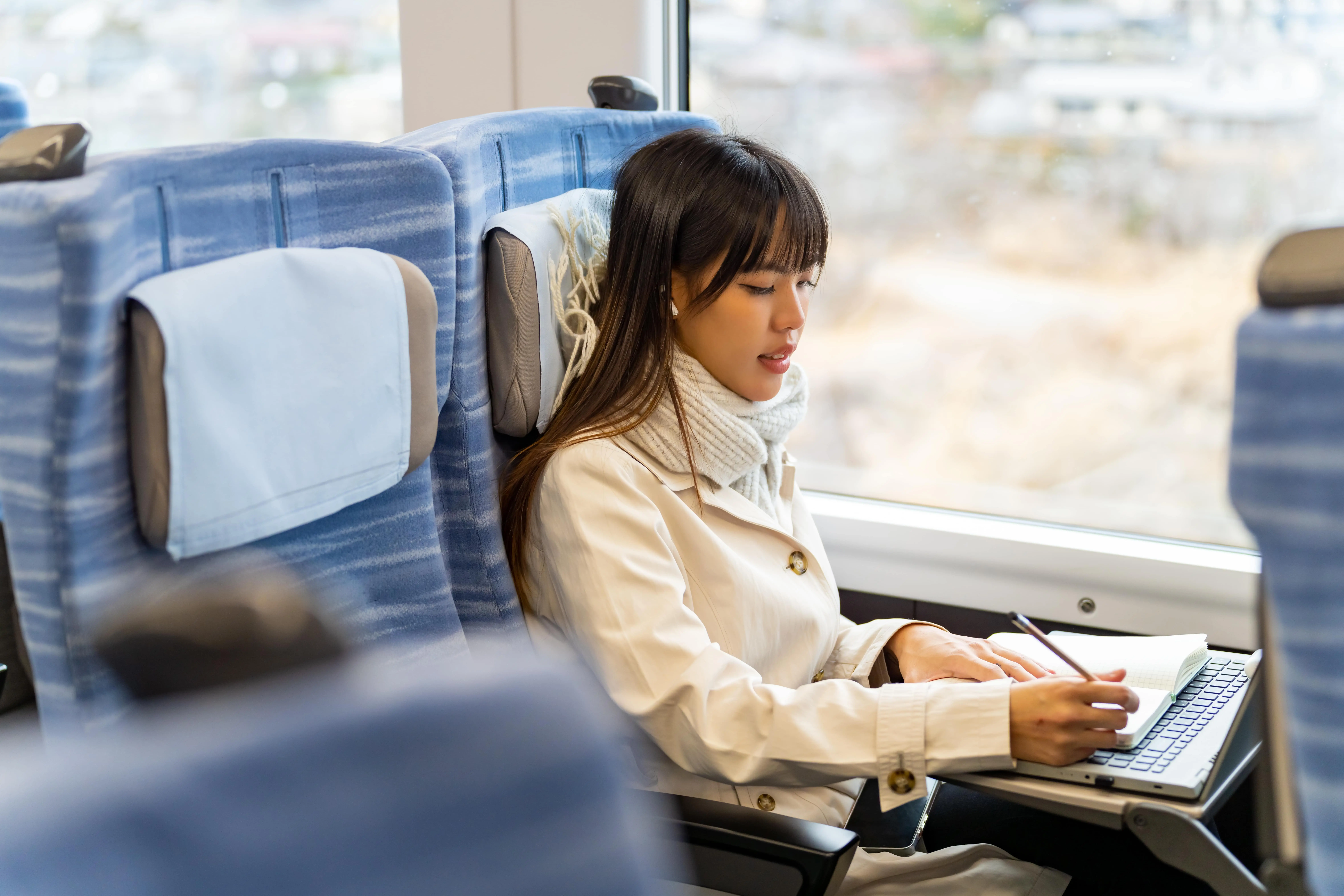 Train Books: A young woman writes on a notepad at her seat on a train.