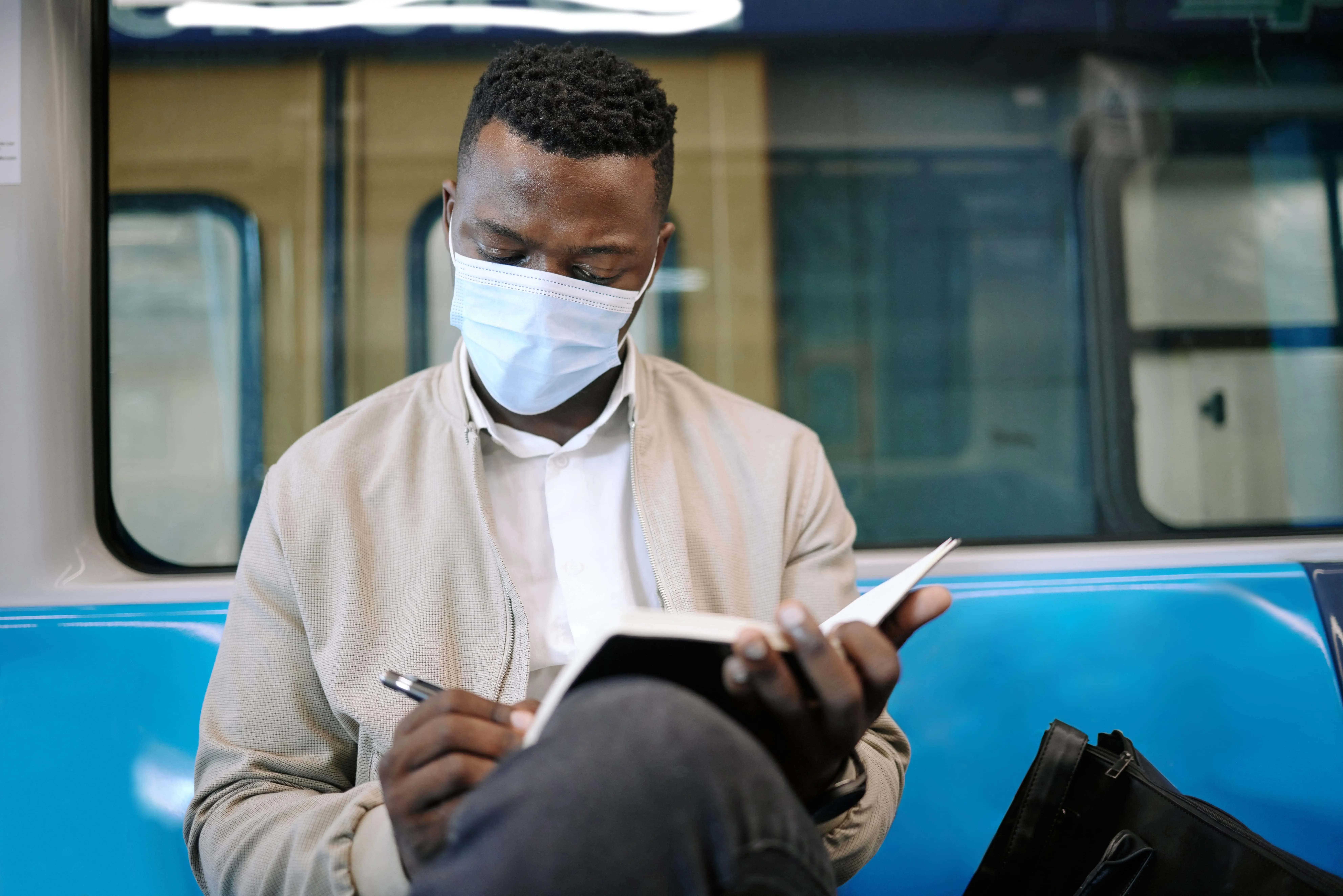 Train Books: A young masked man writes in a notepad whilst travelling on board a train.