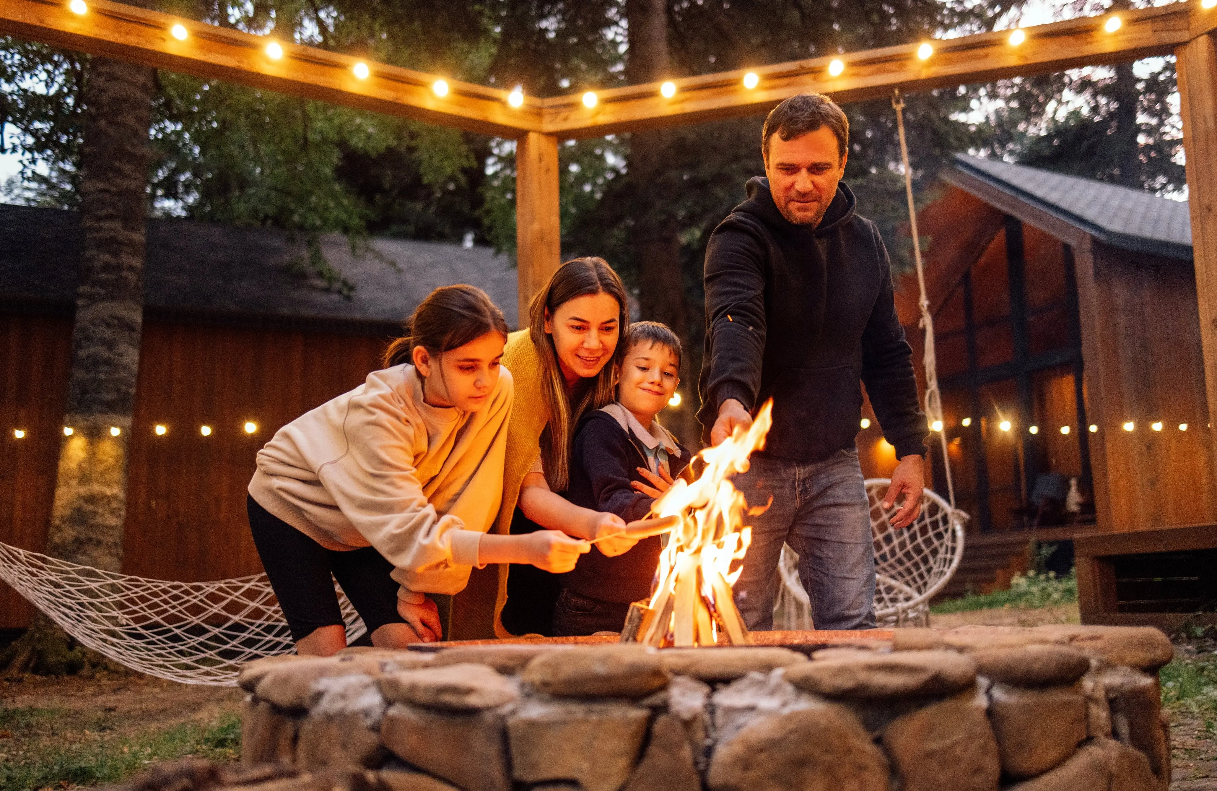 A young married couple with children roasts marshmallows on the fire in in the backyard of the house.