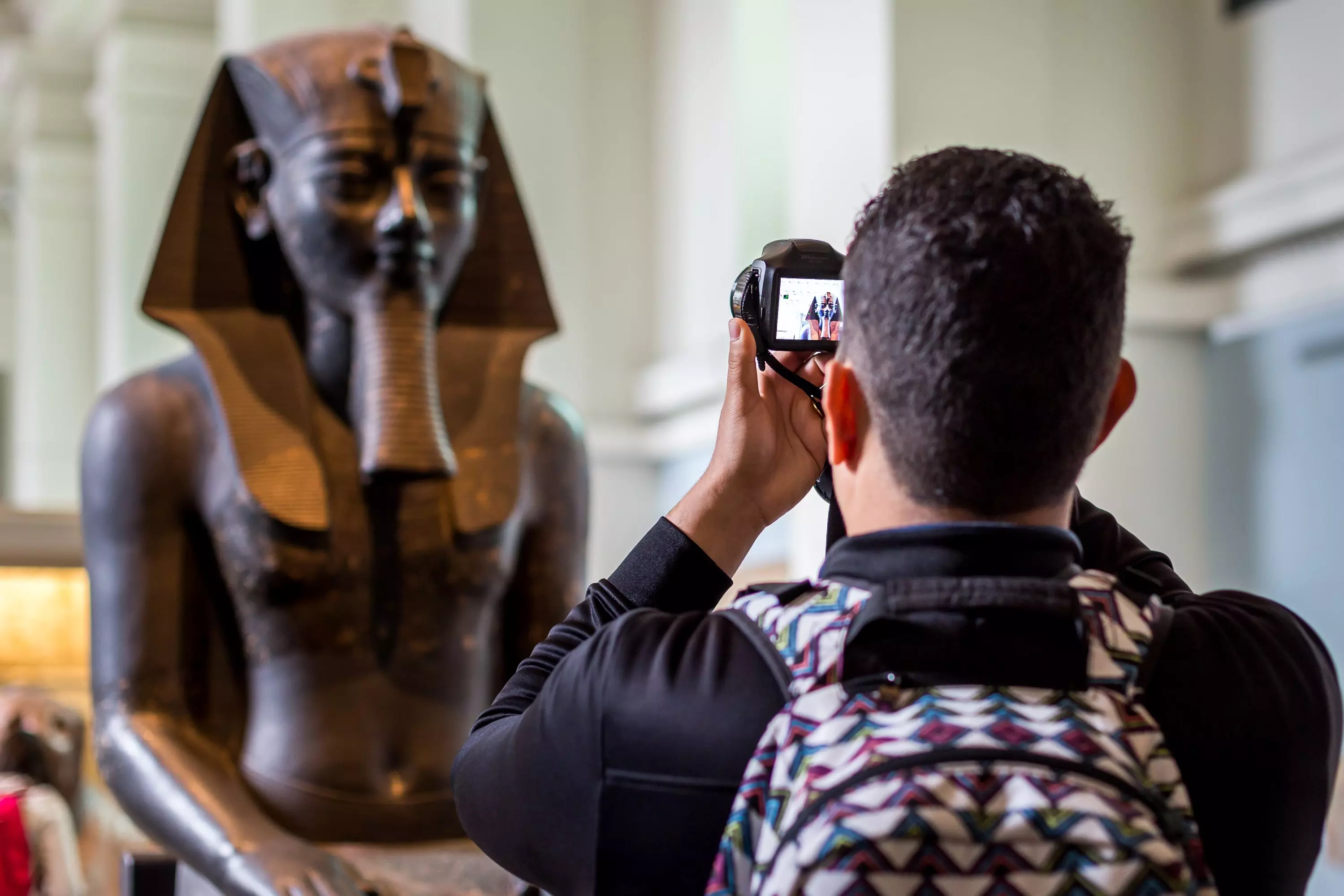 A man taking a photo of a statue of an Egyptian pharaoh